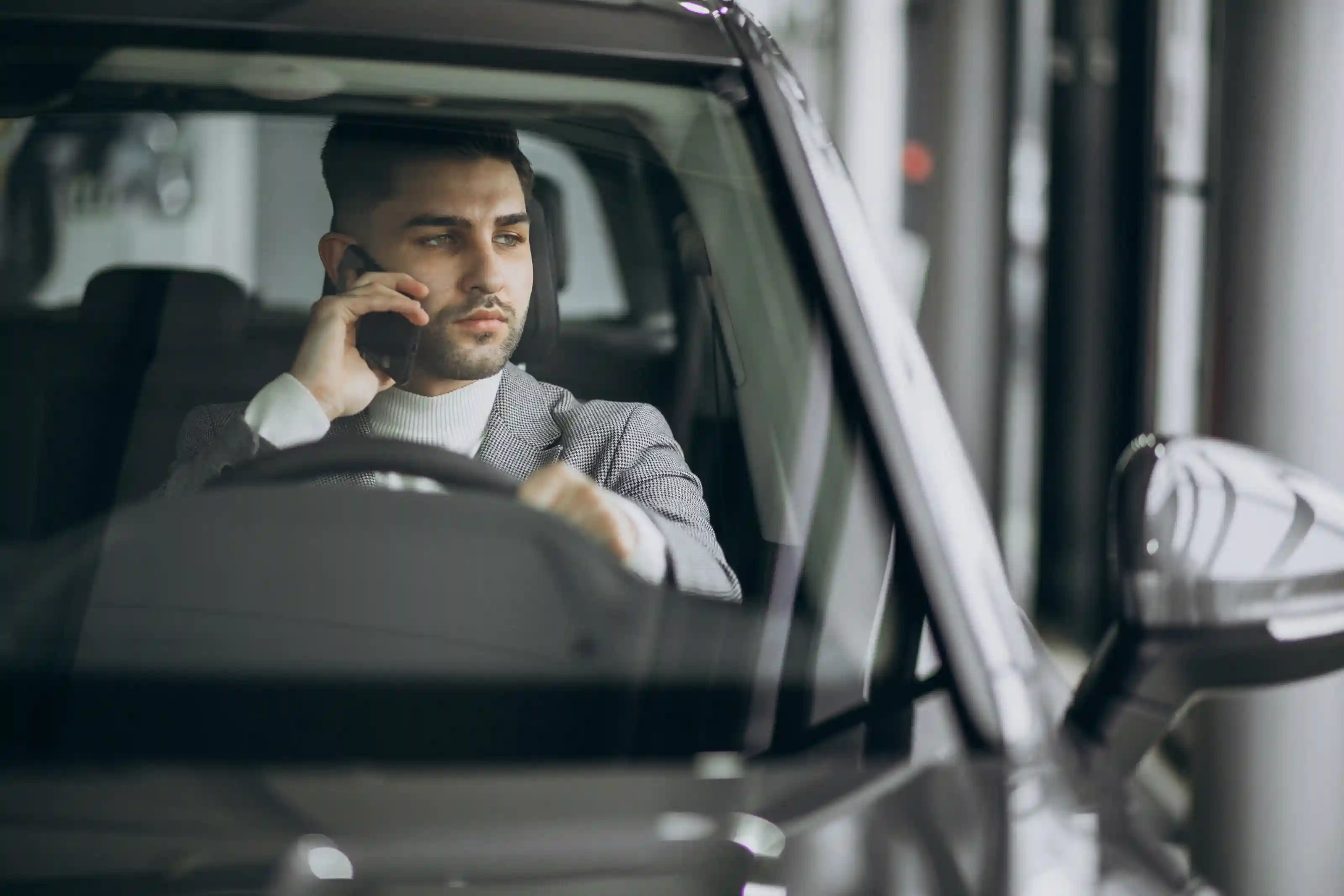 Business professional sitting in the driver's seat of a luxury car while making a phone call.